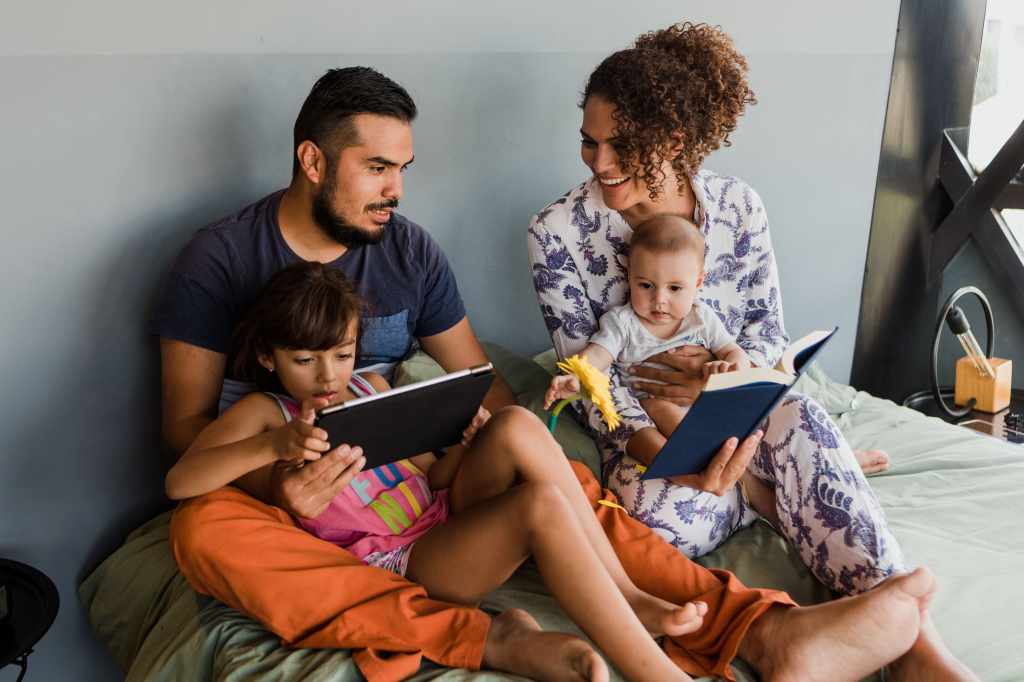 Família com duas crianças pequenas a utilizar o computador portátil na cama
