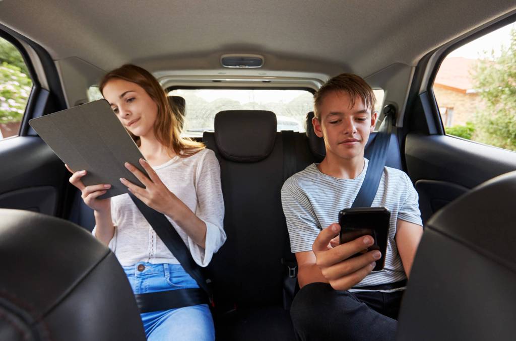 Foto de adolescentes no banco de trás de um carro a olhar para os seus dispositivos móveis.